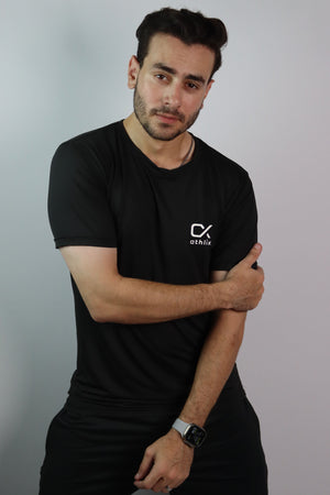 A man wearing a black crew-neck t-shirt with a white 'CX STITCH' logo on the left chest, paired with black pants, posing against a light gray studio background.
