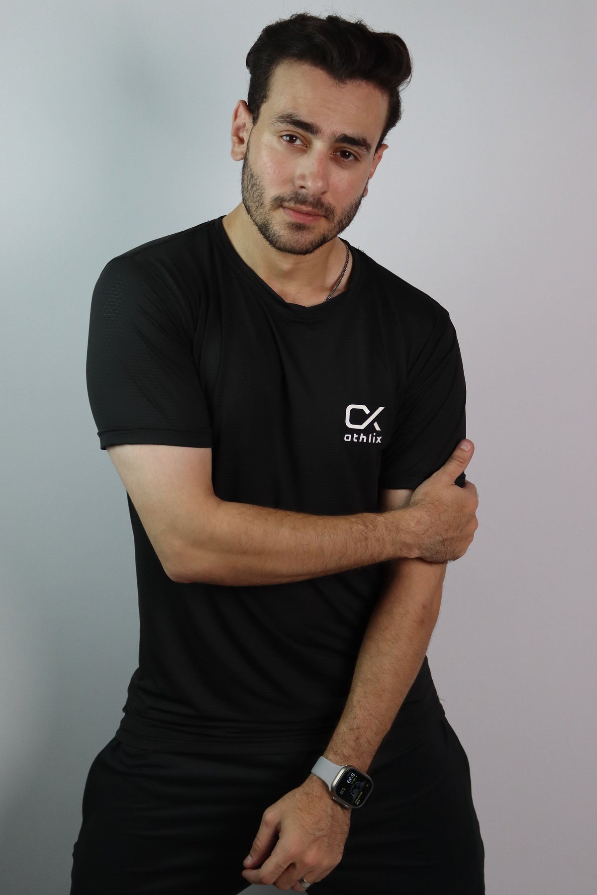 A man wearing a black crew-neck t-shirt with a white 'CX STITCH' logo on the left chest, paired with black pants, posing against a light gray studio background.
